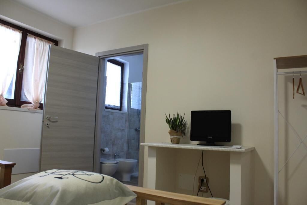 A room with a bed, a TV on a stand, a window with curtains, and a door leading to a bathroom.