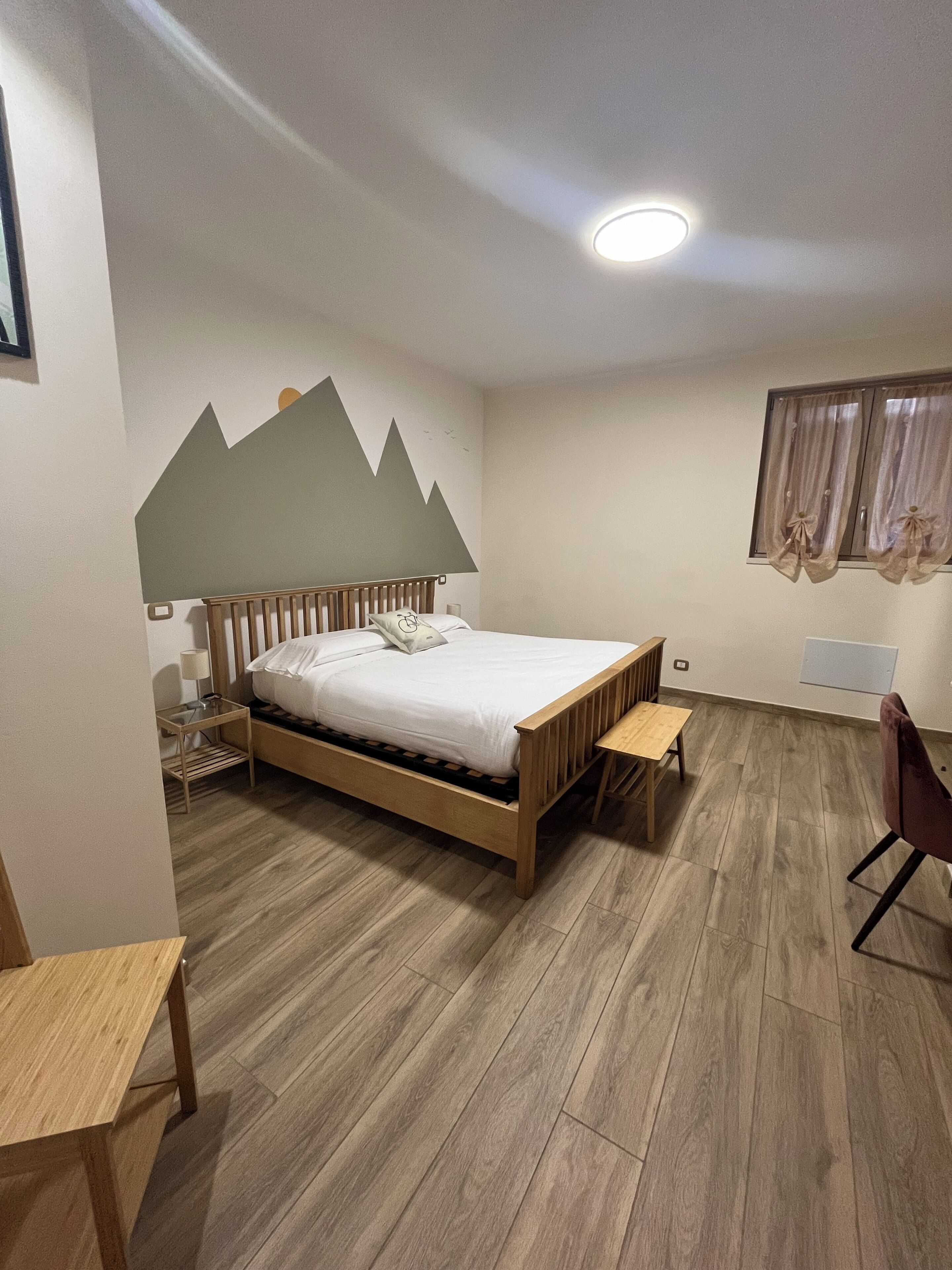 A bedroom with a wooden bed, a bedside table, a chair, and a desk.