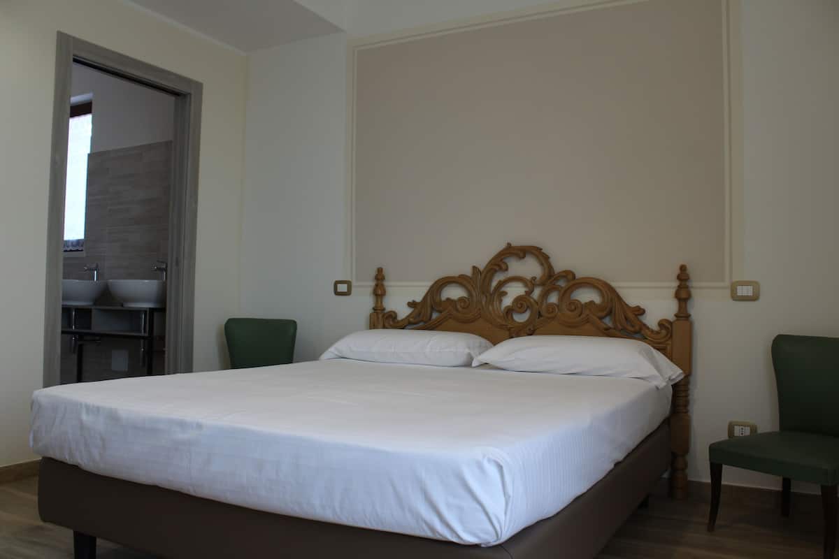 A bedroom with a large bed, two chairs, and a wooden headboard.