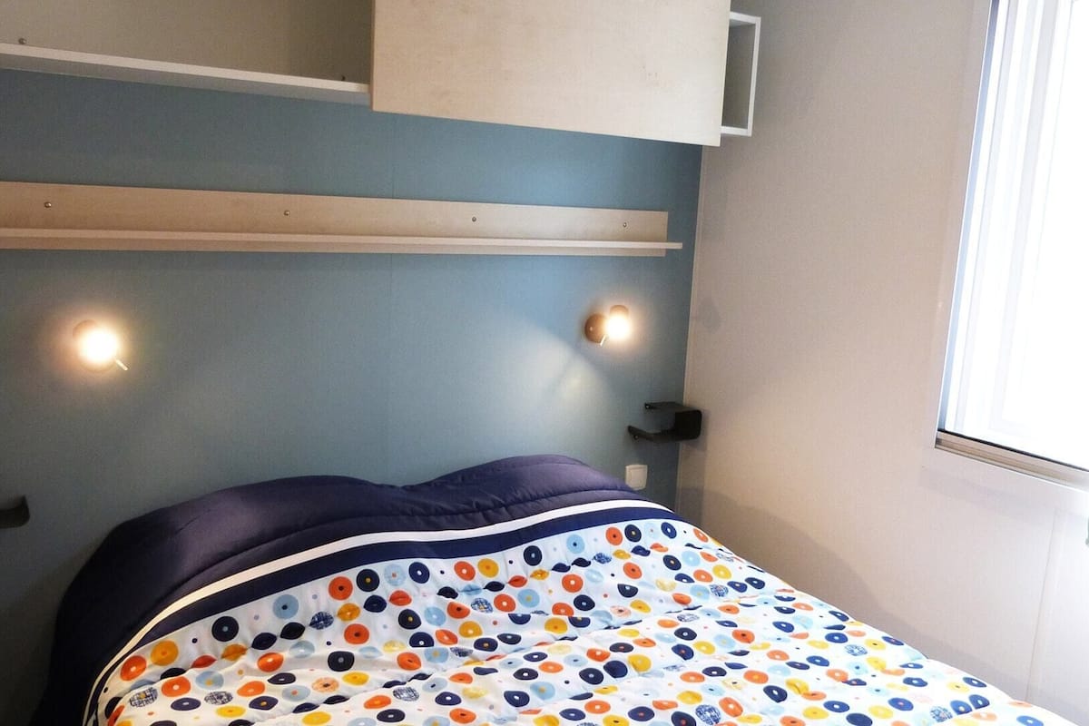 Una cama con un colorido edredón de lunares, un cabecero con repisas incorporadas y dos lámparas fijadas a la pared.