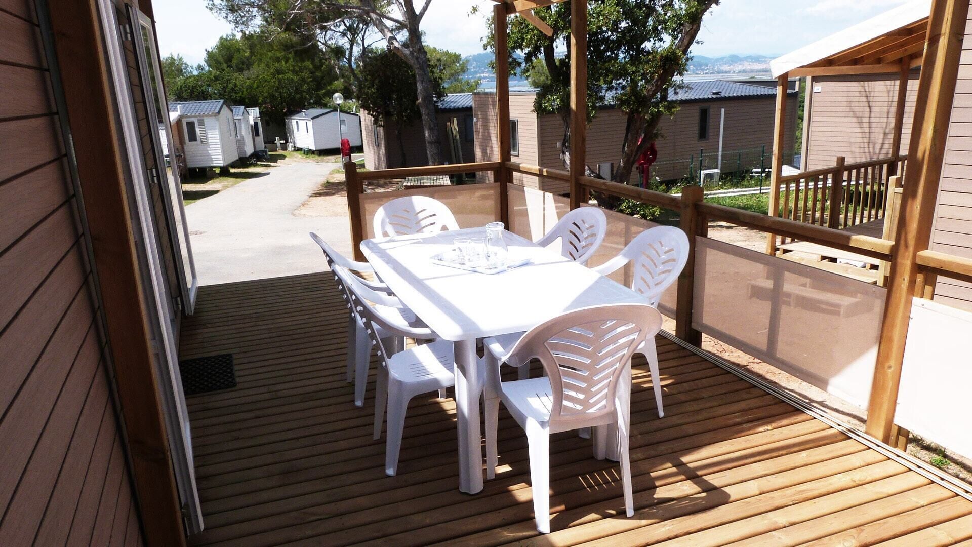 Een houten terras met een witte tafel en stoelen, met uitzicht op een rij stacaravans.