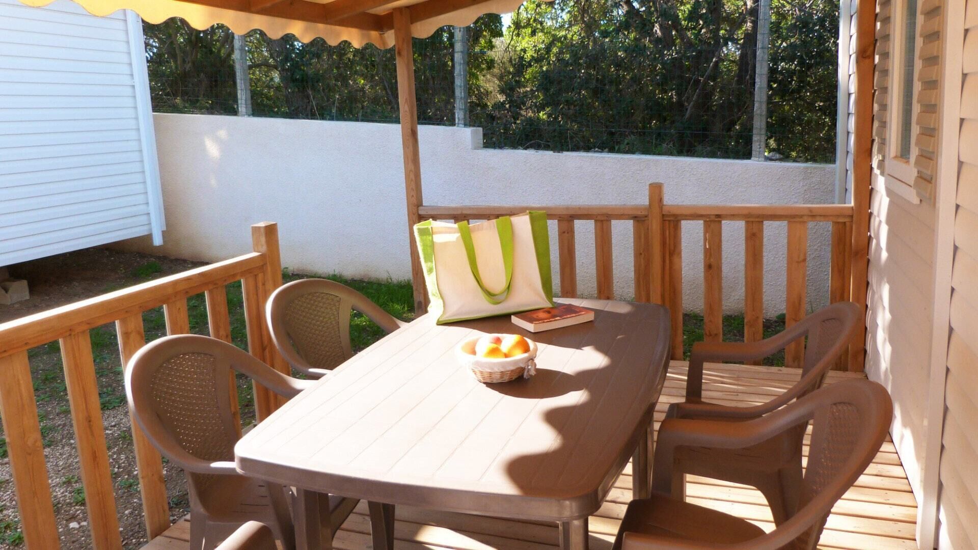 Une terrasse en bois avec une table et des chaises, un panier de fruits et un sac fourre-tout.