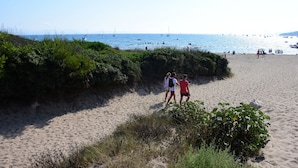 Ein sandiger Strand mit vereinzelter Vegetation und freiem Blick auf das Meer.