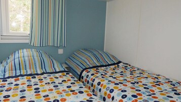 Ein Zimmer mit zwei Betten, beide mit gestreifter Bettwäsche und einem Punkte-Muster. Es gibt ein Fenster mit Vorhang, und die Wände sind hellblau gestrichen.
