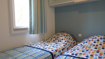 Una habitación con dos camas, cada una con una colcha de lunares y rayas. Hay una ventana con cortina, y las paredes están pintadas de un color claro.