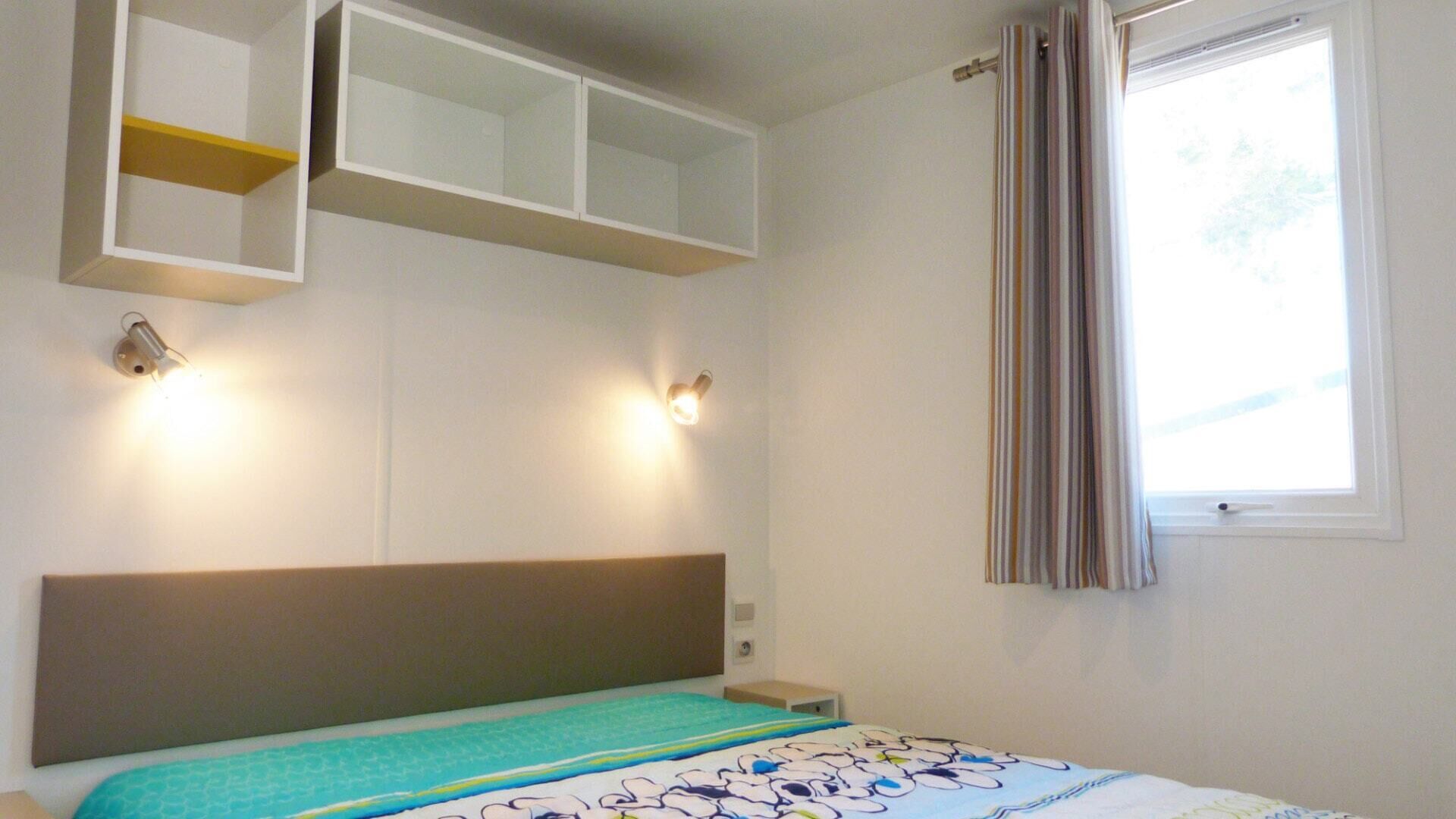A bedroom with a bed, a headboard, a window with curtains, and built-in shelves above the bed.