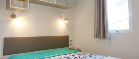 A bedroom with a bed, a headboard, a window with curtains, and built-in shelves above the bed.