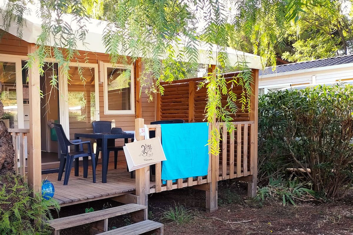 Una terraza de madera con una mesa, sillas y un espacio de estar techado, además de un toldo azul.