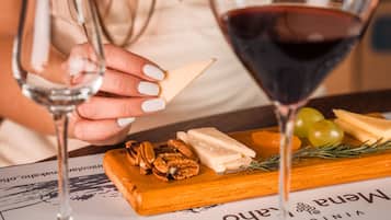 Una mesa con una copa de vino tinto, otra copa con un poco de vino y una tabla de quesos con varios quesos y nueces.
