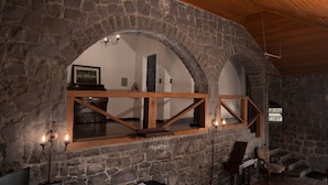 A stone-walled room with a wooden ceiling, a wooden-framed window, and a chandelier.