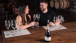 A couple seated at a wooden table with multiple wine glasses and a bottle of champagne.