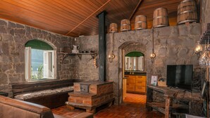 A rustic interior with stone walls, wooden beams, a brick fireplace, a seating area, and a television. - Casa de Pedra Mena Kaho (Bento Gonçalves)