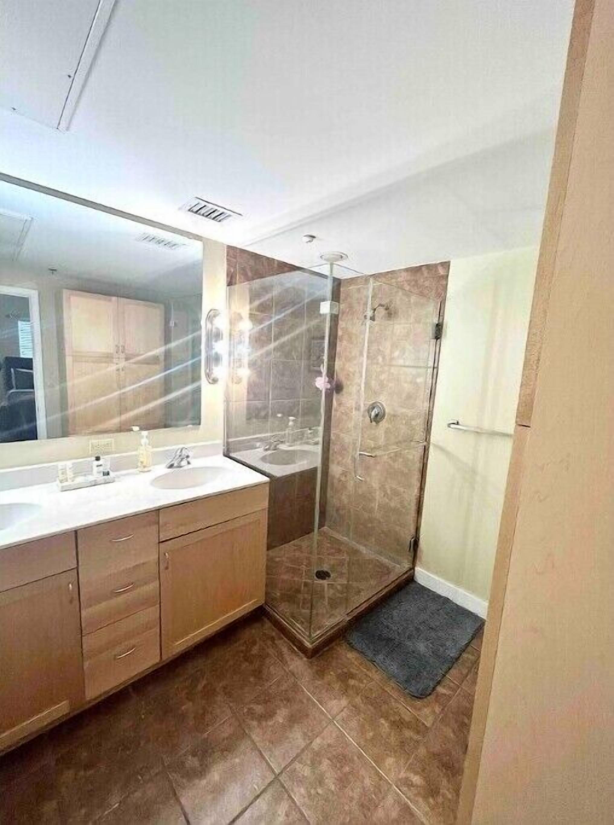 Een moderne badkamer met een douche met glazen wand, een grote spiegel en een wastafelmeubel met wastafel en kast.