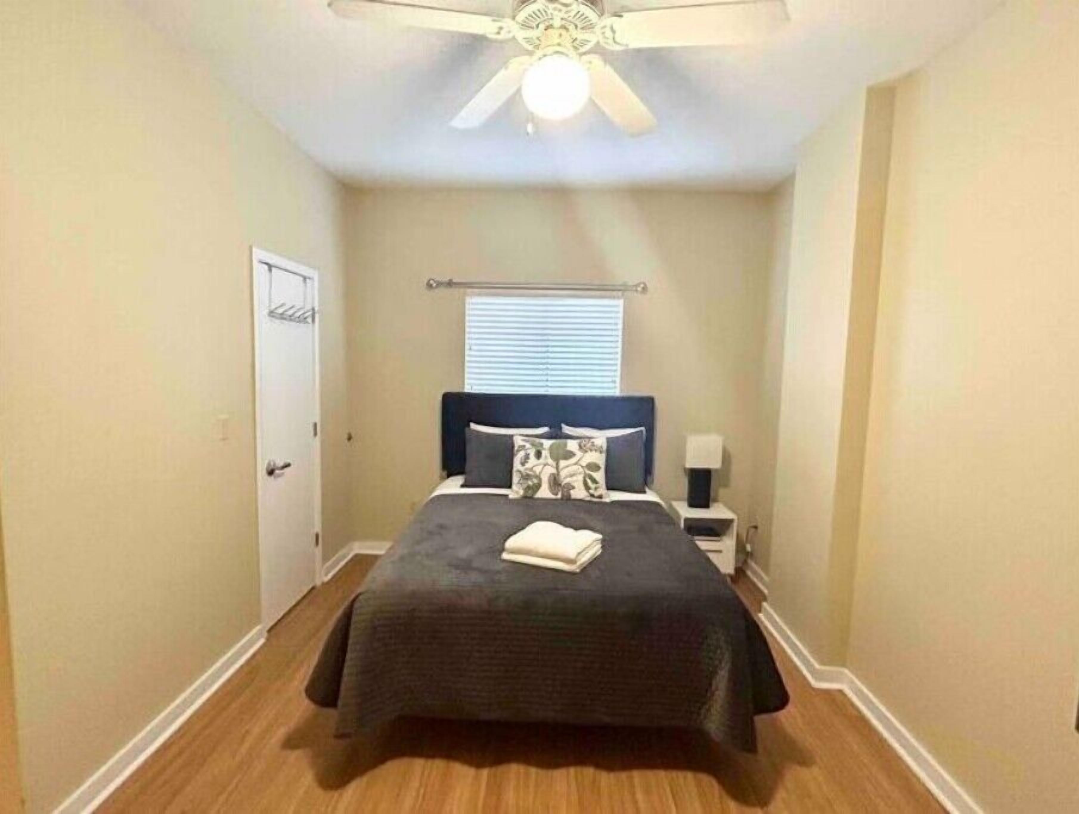 Une chambre à coucher comprenant un lit, une table de chevet, un ventilateur de plafond et une fenêtre avec des stores.