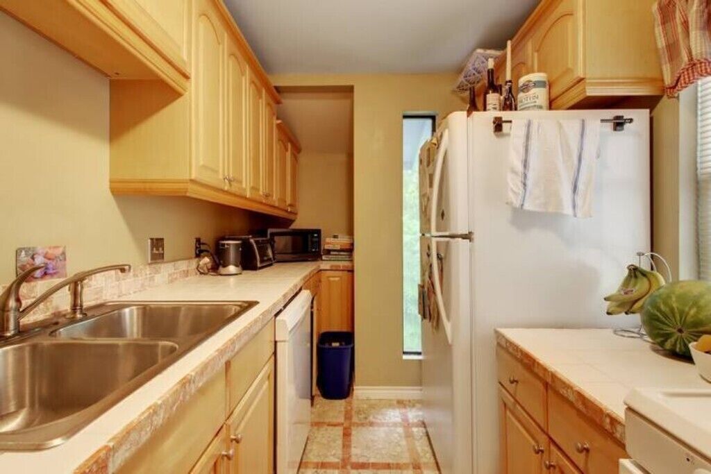 A compact kitchen with wooden cabinets, a stainless steel sink, a refrigerator, and a microwave.