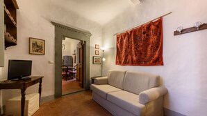 A living room with a beige sofa, a television on a wooden table, and a red tapestry on the wall. - Casa torre via de' Neri by Mmega (Florence)