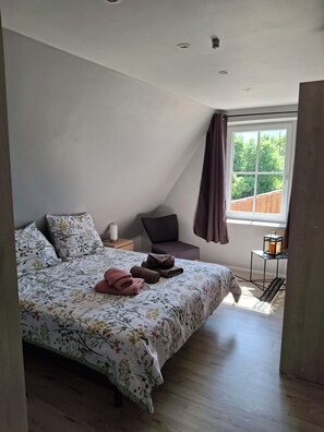 A bedroom with a bed, pillows, a bedside table, a chair, a window, and a nightstand.