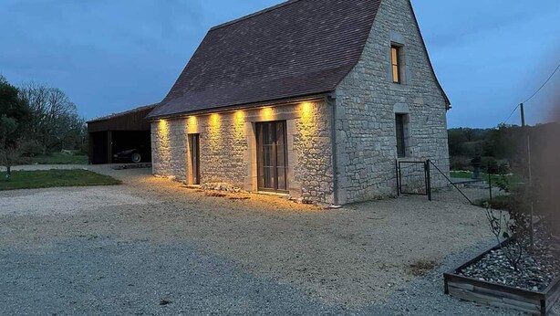 Une construction en pierre avec un toit en pente, un garage et une allée gravillonnée.