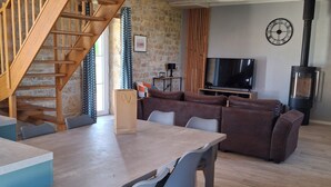 Un vaste espace de vie comprenant un escalier en bois, une table à manger avec des chaises, un canapé, un téléviseur et une cheminée.