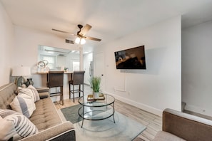 A modern living room with a sofa, a coffee table, a TV mounted on the wall, and a ceiling fan.