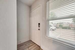 A narrow hallway with a white door, a window with blinds, and a wooden floor. - I69 - Apt|Patio|11mi to Convention Ctr|Sleeps 2 (Irving)
