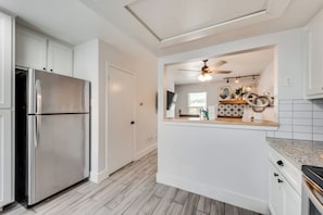 A modern kitchen with a stainless steel refrigerator, white cabinetry, a ceiling fan, and a kitchen island with decorative items.