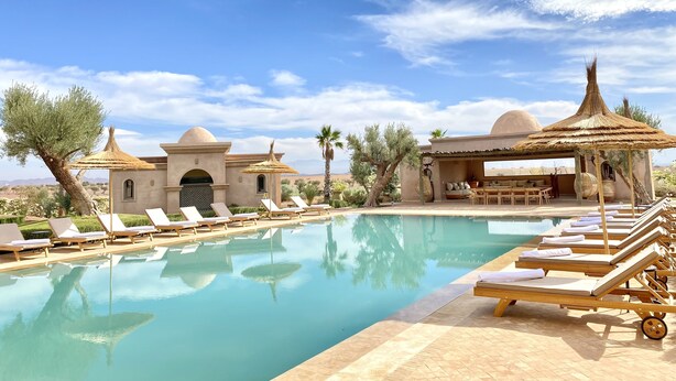 A pool area with lounge chairs, a bar, and a thatched-roof structure.