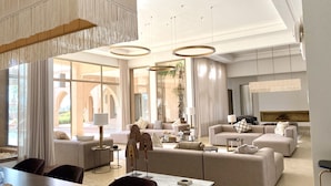 A spacious living room with a large sofa set, a dining table, and a TV mounted on the wall.