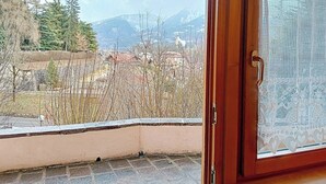 Blick von einem Balkon mit einer Holztür und Spitzenvorhang auf eine Stadt mit Bergen im Hintergrund.