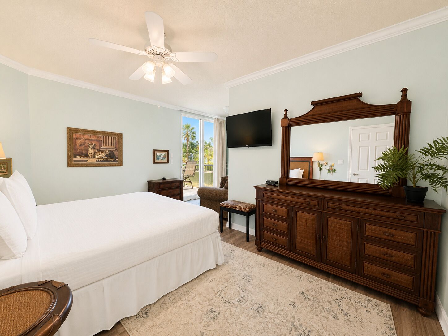 Une chambre à coucher comprenant un lit, une commode, un ventilateur de plafond, une télévision et une vue sur l’extérieur.