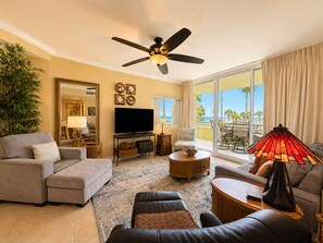 Ein Hotelzimmer mit einer Couch, einem Sessel, einem Fernseher, Deckenventilator und Blick auf den Strand.