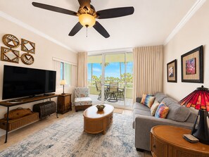 A living room with a flat-screen TV, a ceiling fan, a sofa, a coffee table, and a balcony with a view.