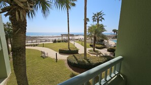 A balcony with a view of a beach, palm trees, and a pool area.