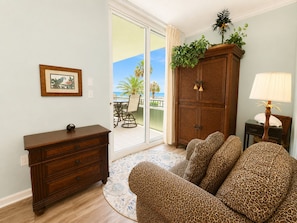 A living room with a sofa, a wooden cabinet, a lamp, and a view of the outdoors.