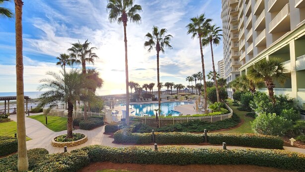 A resort with a pool, palm trees, and a view of the beach.