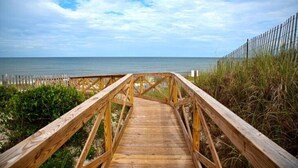 A wooden boardwalk leading to the beach with a fence on the right.