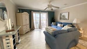 A living room with a blue sofa, a white cabinet, a ceiling fan, and a large window with curtains.