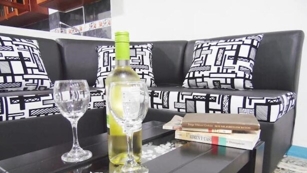 A black sofa with patterned cushions, a glass table with a wine bottle and two glasses, and a stack of books. - Central and Private 1km From the Hacienda Naples (Antioquia)