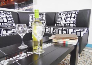 A black sofa with patterned cushions, a glass table with a wine bottle and two glasses, and a stack of books. - Central and Private 1km From the Hacienda Naples (Antioquia)