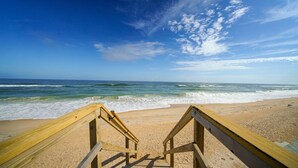 A wooden boardwalk leading to a sandy beach with ocean waves.