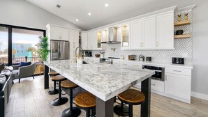 A modern kitchen with white cabinetry, a marble island, and bar stools.