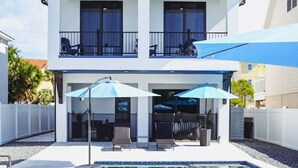 A two-story modern house with a swimming pool, outdoor seating, and a covered patio.