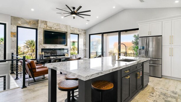 A modern kitchen with a large island, stainless steel appliances, and a TV mounted on the wall.