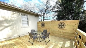 Une terrasse en bois avec une table et des chaises, entourée d’une clôture en bois agrémentée de panneaux décoratifs.