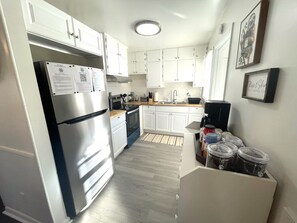 Una cocina compacta con armarios blancos, un refrigerador de acero inoxidable, un microondas y una cafetera.