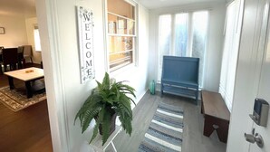 Un salon moderne avec une cheminée, une pancarte « BIENVENUE », une plante en pot et un tapis à rayures.