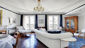 Een ruime woonkamer met een witte bank, een houten kast en een kroonluchter.