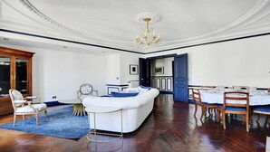 Een ruime woonkamer met een witte bank, houten stoelen en een eethoek met een tafel voor zes personen.