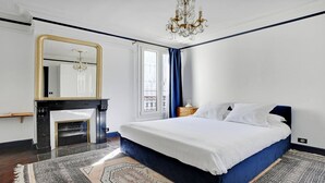 Een slaapkamer met een groot bed, een open haard, een spiegel en een kroonluchter.