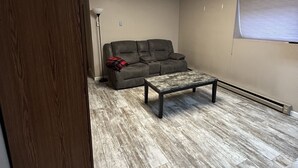 A room with a wooden floor, a grey sofa, and a small table. - Cozy Bach Suite  (Winifred)